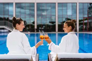 Due donne in accappatoio bianco tengono in mano dei drink.