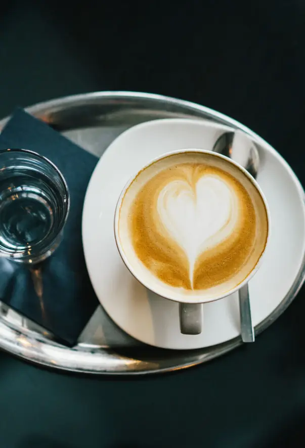 Tazza di caffè con schiuma a forma di cuore su un piatto bianco.