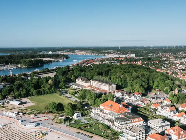 Veduta aerea di una città con edifici e alberi, con un accenno di acqua visibile.