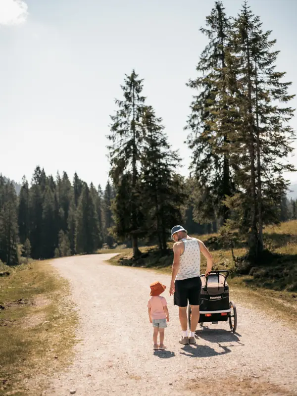 Un uomo e un bambino camminano su un sentiero di ghiaia, circondati da alberi.