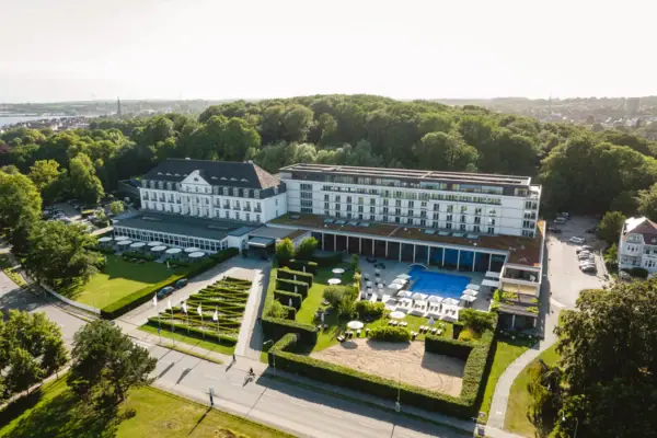 Hotel benessere A-ROSA Travemünde Il grande edificio bianco del centro termale, con una piscina e degli alberi.