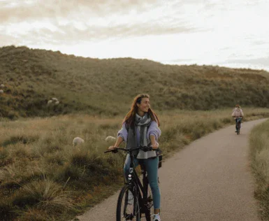 Donna in bicicletta su un sentiero circondato da erba e colline.