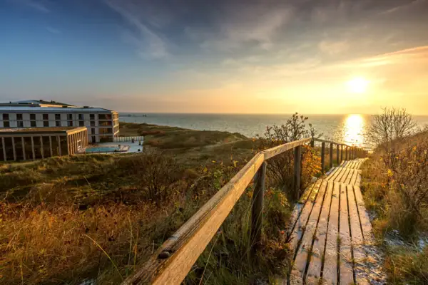 Holzsteg, der zu einem Strand führt, umgeben von Himmel und Wolken.