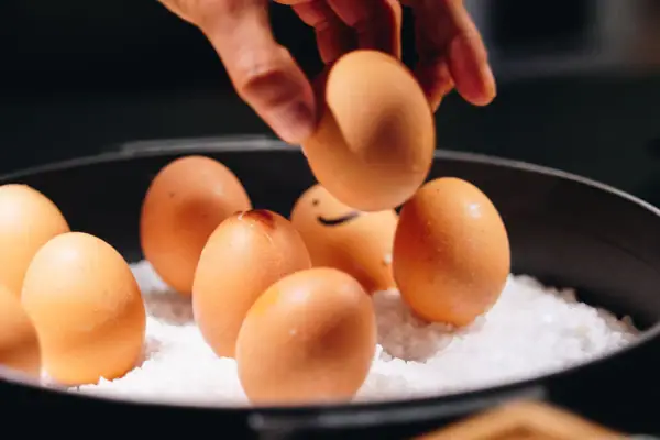 Eine Hand greift nach einem Ei in einer Schale mit Salz.