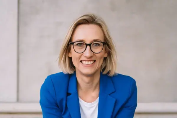 Una donna in abito blu seduta sui gradini sorridente.