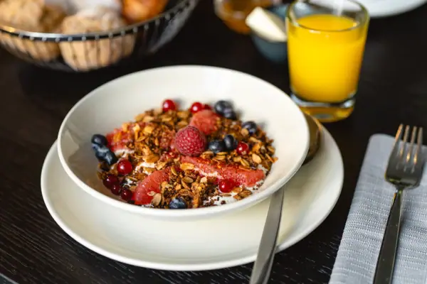 Una ciotola di frutta e muesli accanto a un bicchiere di succo di frutta.