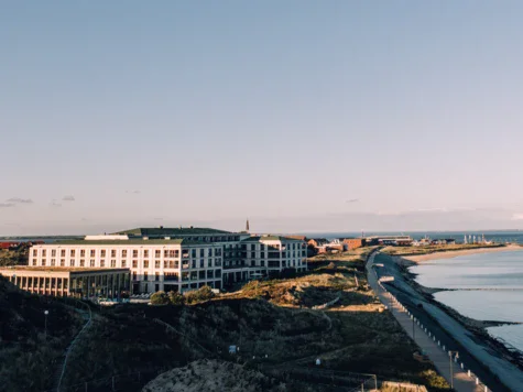 Edificio adiacente a un corpo d'acqua con cielo sereno e spiaggia visibile.