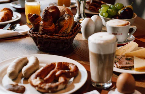 Tavolo apparecchiato con varietà di cibi e bevande, inclusi piatti, tazze e stoviglie.