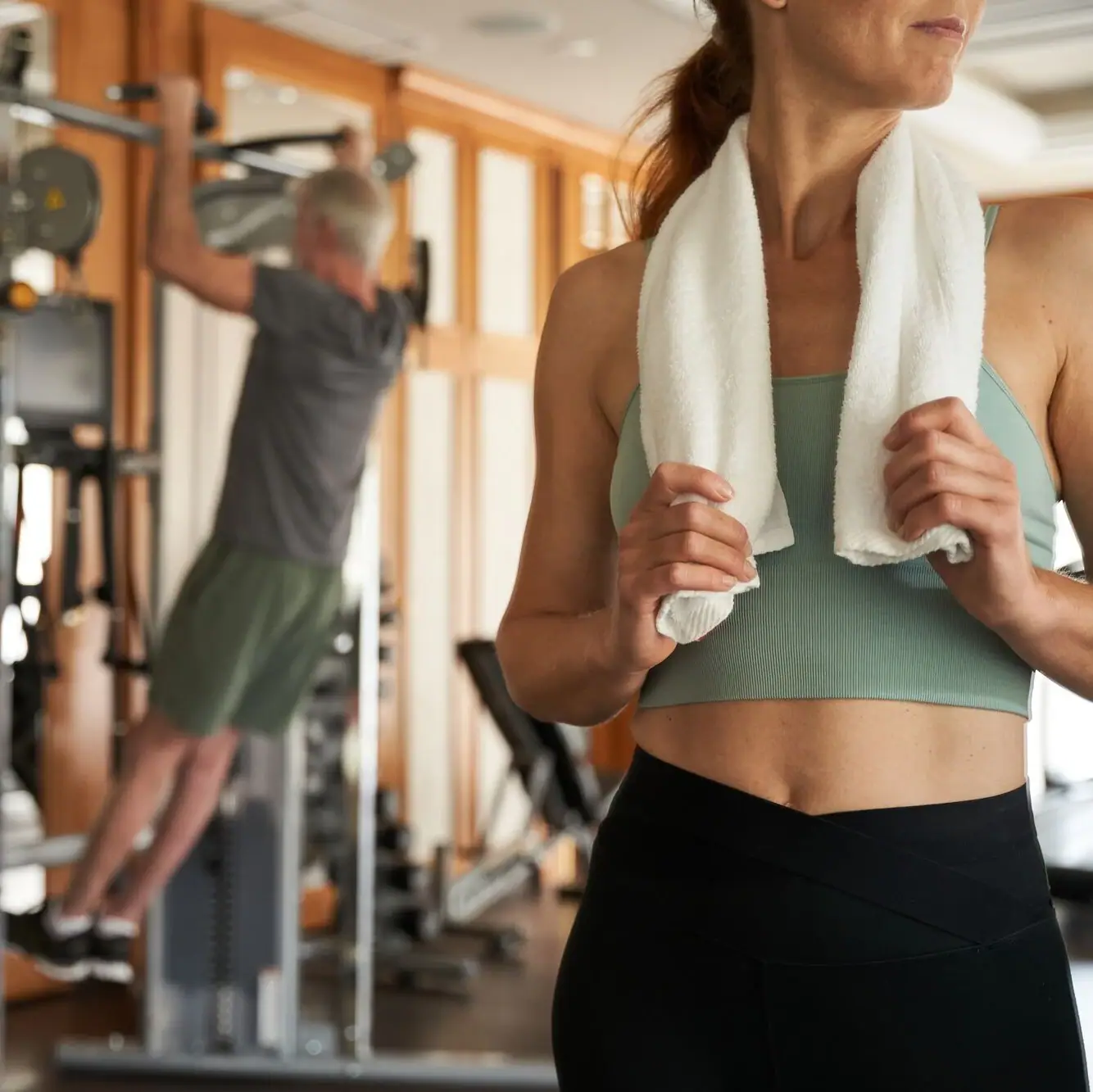 Frau hält ein Handtuch um den Nacken im Fitnessstudio.