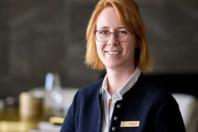 Eine Frau mit Brille und blauer Jacke lächelt.