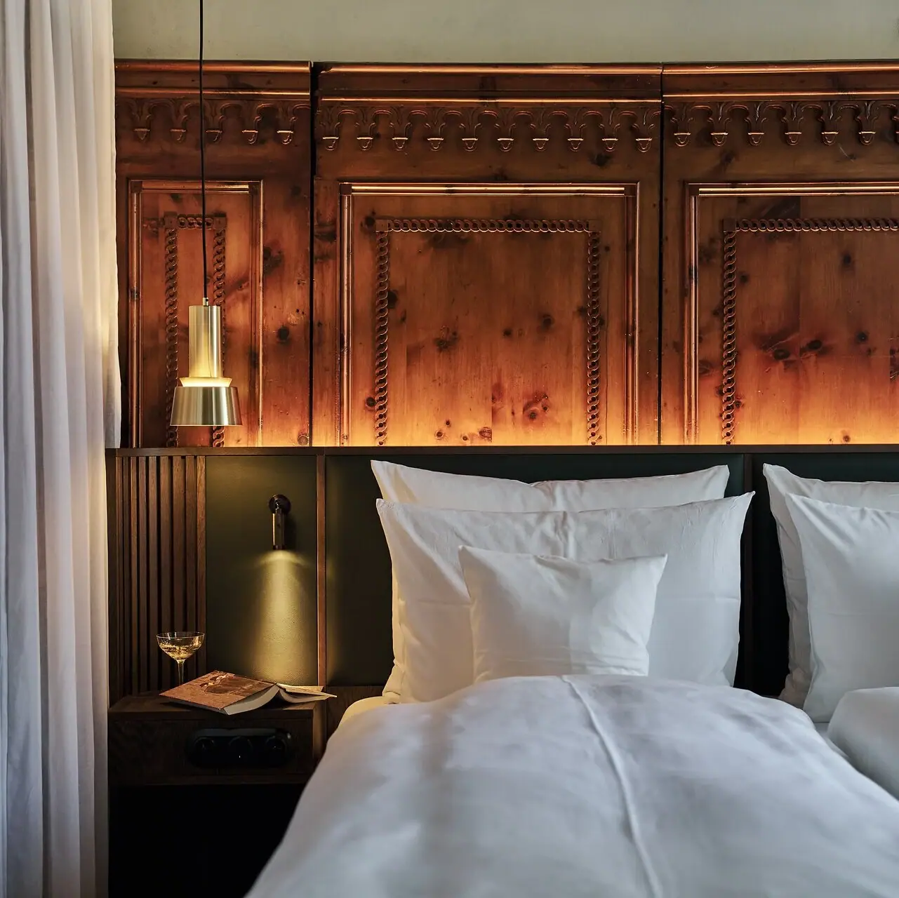 Un letto con cuscini bianchi e una lampada a fianco.