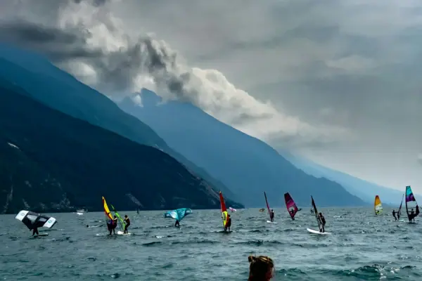 Windsurfisti al largo di Torbole Un gruppo di persone su tavole da windsurf in acqua, con le montagne sullo sfondo.
