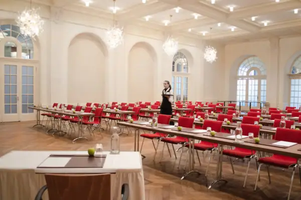Ein großer Tagungsraum mit Tischen und roten Stühlen.