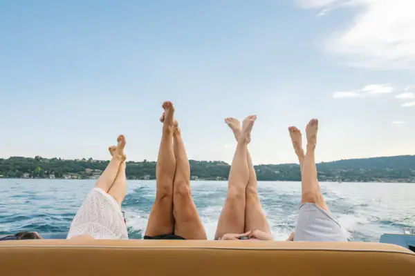 Vier Frauen strecken ihre Beine vom Boot aus über den Gardasee.