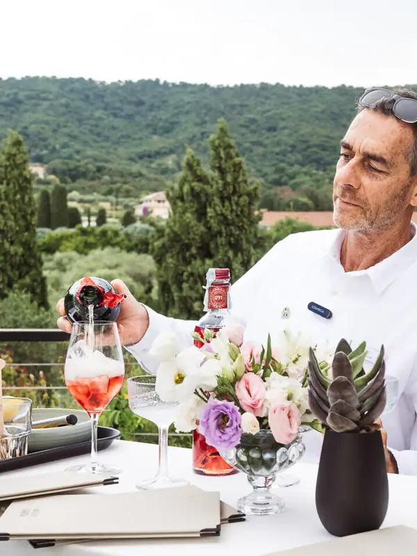 Un uomo in piedi accanto a un tavolo con una bottiglia di vino e fiori.