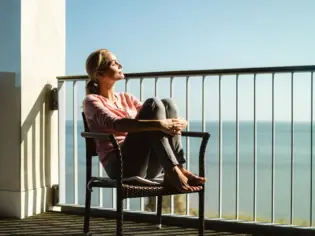 Una donna siede su una sedia in balcone e si gode il sole.