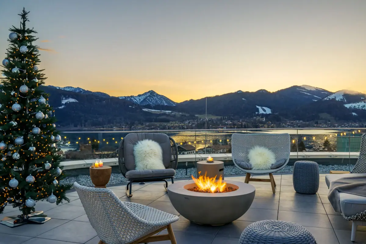 La terrazza dell’A-ROSA Tegernsee, con un focolare, sedie e, sullo sfondo, la vista sulle montagne innevate.