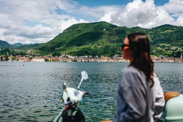 Gardasee Eine Frau sitzt auf einem Roller und blickt auf ein Gewässer.