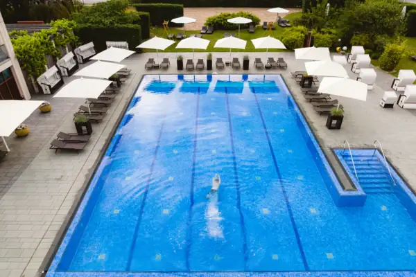 SPA-ROSA Travemünde Eine Person schwimmt in einem Außenpool mit Liegen und Sonnenschirmen darum.