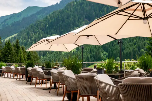 Mehrere gemütliche Stühle und Sonnenschirmen auf einer Terrasse mit Bergen im Hintergrund.