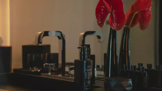 Un elegante lavabo nero con rubinetto argentato e un vaso scuro con un fiore rosso. 