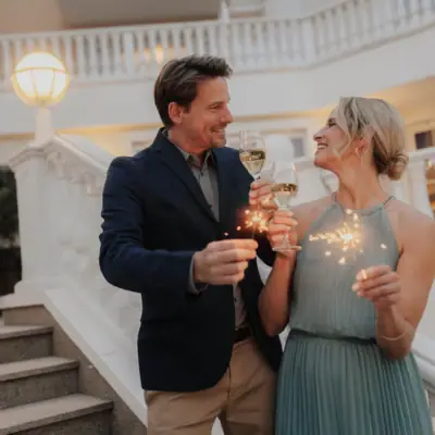 Un uomo e una donna tengono in mano dei bicchieri da vino e sorridono.