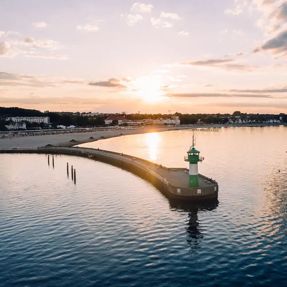 Travemünde Un molo con un faro su di esso, circondato da acqua e cielo nuvoloso.