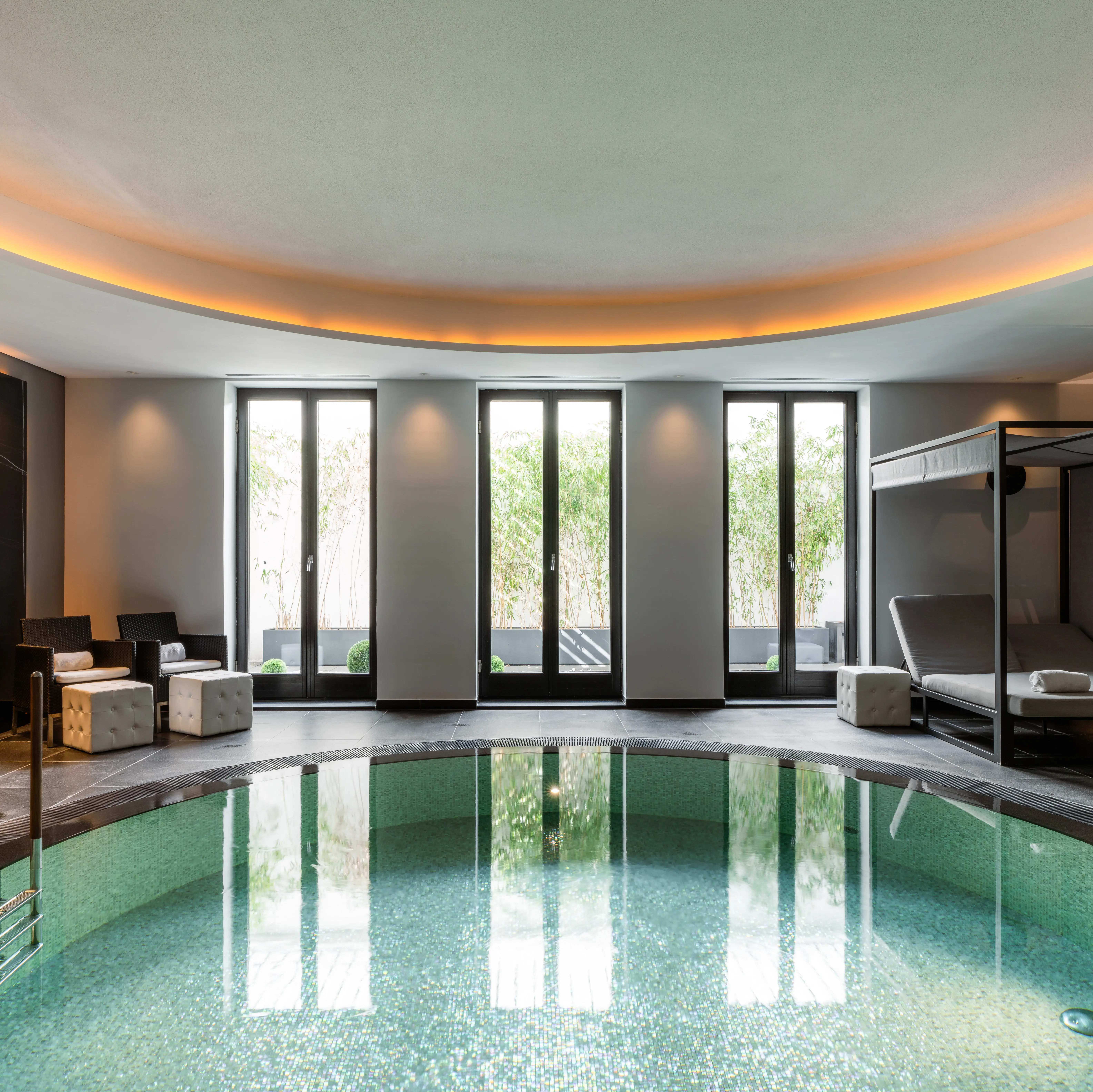 Ein runder Pool mit blauem Wasser vor einer Fensterwand mit Blick ins Grüne.