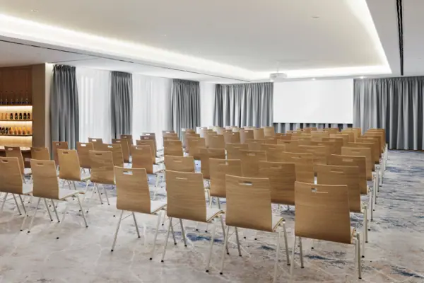 Conferenza 1 A-ROSA Tegernsee La sala conferenze 1 dell'A-ROSA Tegernsee, dotata di file di sedie, un proiettore e uno schermo.