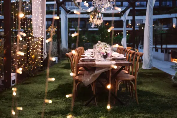 Ein Tisch für eine Dinnerparty gedeckt, mit Kerzen und Beleuchtung. Perfekt für eine Hochzeitsfeier im Garten.