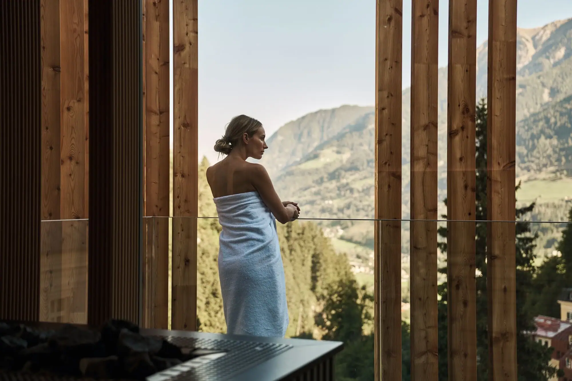 Una donna in un asciugamano bianco davanti a una finestra con vista su una valle.