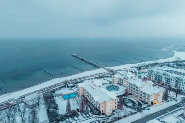Spiaggia innevata con edifici e molo in inverno.