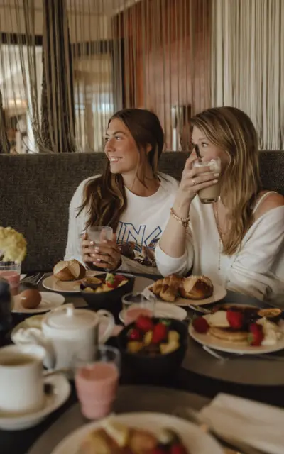 Due donne sedute a un tavolo mentre mangiano e bevono caffè in un ambiente interno.