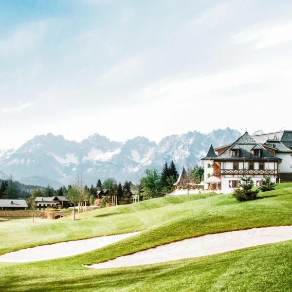 Campo da golf con un edificio sullo sfondo, circondato da alberi e prato verde.