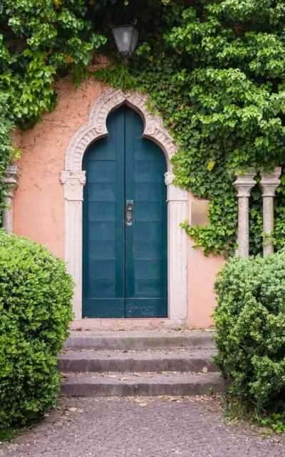 Porta con arco in pietra e vialetto in pietra circondato da arbusti.