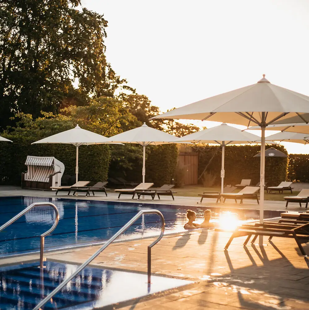 A-ROSA Travemünde Eine Person im Pool mit Sonnenschirmen und Liegestühlen.