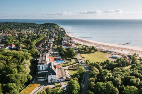 Vista aerea di una spiaggia e di una città con edifici circondati da alberi e acqua.