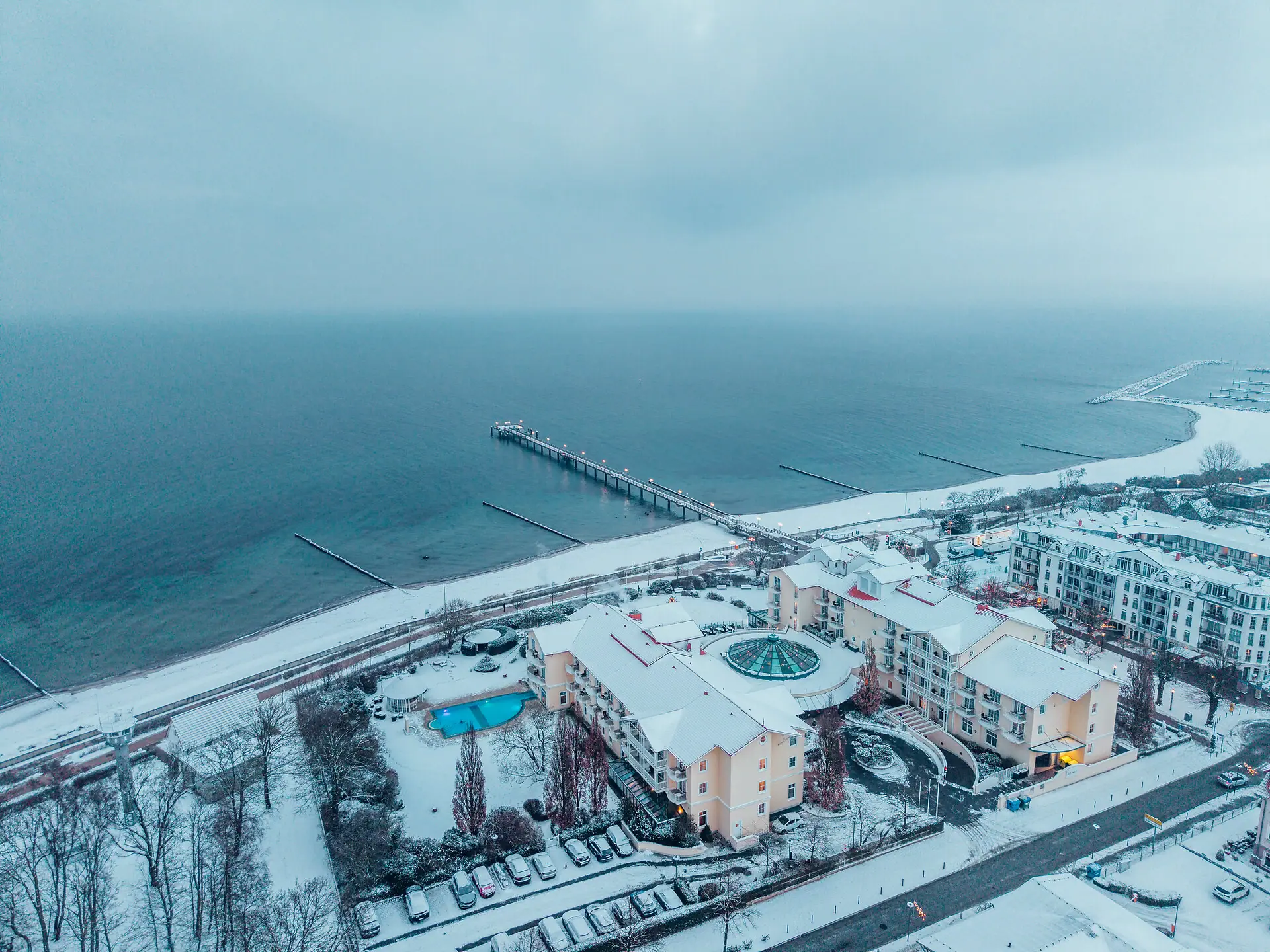 Spiaggia innevata con edifici e un molo in inverno.