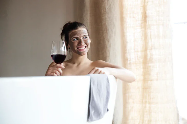 Donna sorridente in una vasca da bagno con un bicchiere di vino.