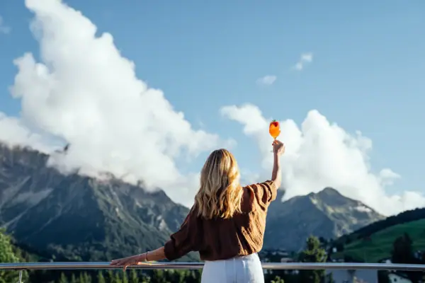 Una donna tiene in mano un drink e guarda verso le montagne.