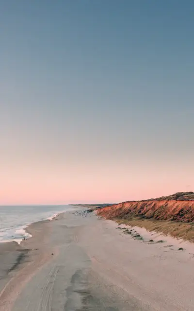 Spiaggia sabbiosa con una scogliera e il mare sullo sfondo.