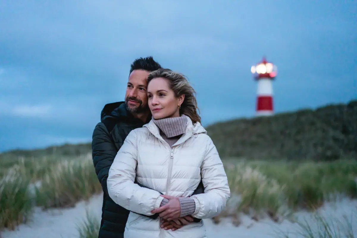 Dune di Sylt Un uomo e una donna sono in piedi sulla spiaggia con un faro sullo sfondo.