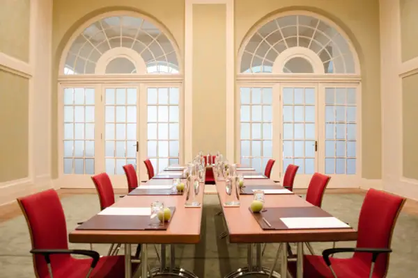 Ein langer Tisch mit roten Stühlen in einem Tagungsraum.