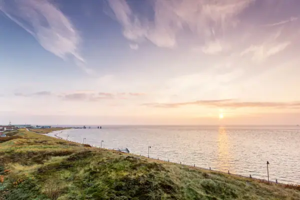 Grüne Hügel neben einem Gewässer unter einem bewölkten Himmel.