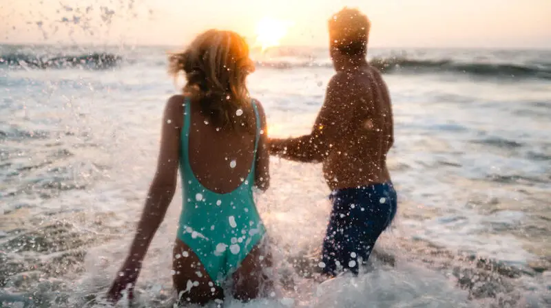 Un uomo e una donna in acqua, indossano costumi da bagno e si divertono in una giornata estiva.