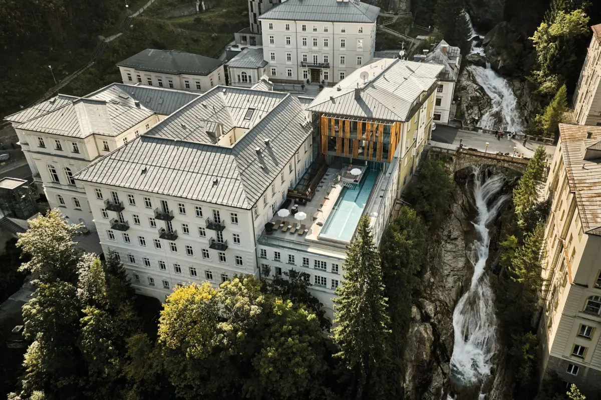 Edificio con piscina e cascata, circondato da alberi.