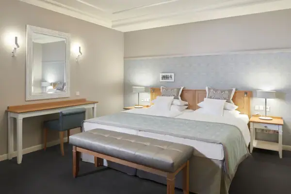 Kurhaus Binz Suite Hotelzimmer mit einem großen gemütlichen Bett und einem Spiegel an der Wand daneben.