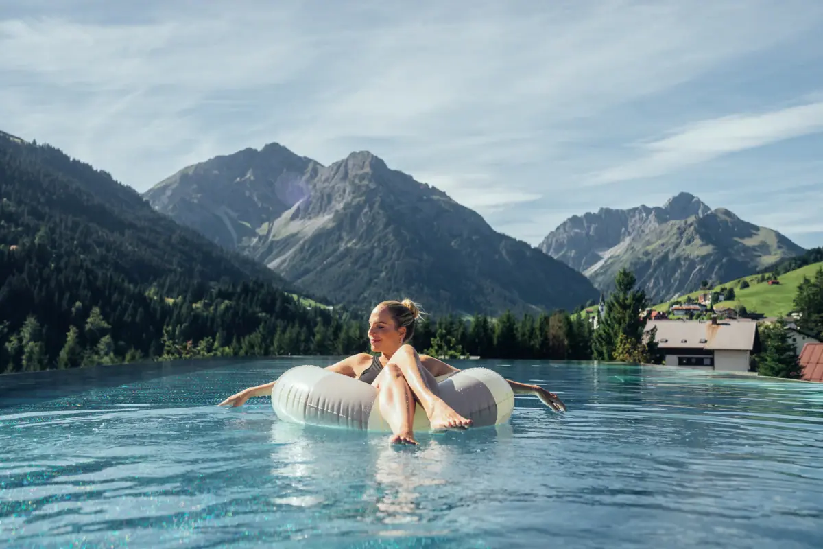 Una donna galleggia su un salvagente in una piscina, con le montagne sullo sfondo.