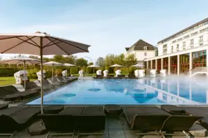 Grande edificio bianco con piscina e alberi in primo piano.