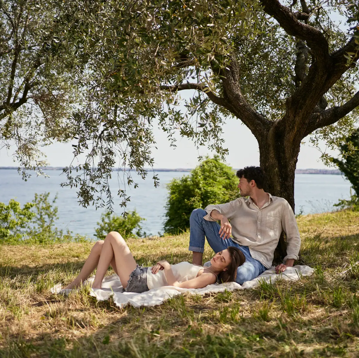 Coppia rilassata all’ombra di un ulivo con vista sul Lago di Garda – momenti di pace e natura durante una passeggiata a San Fermo.